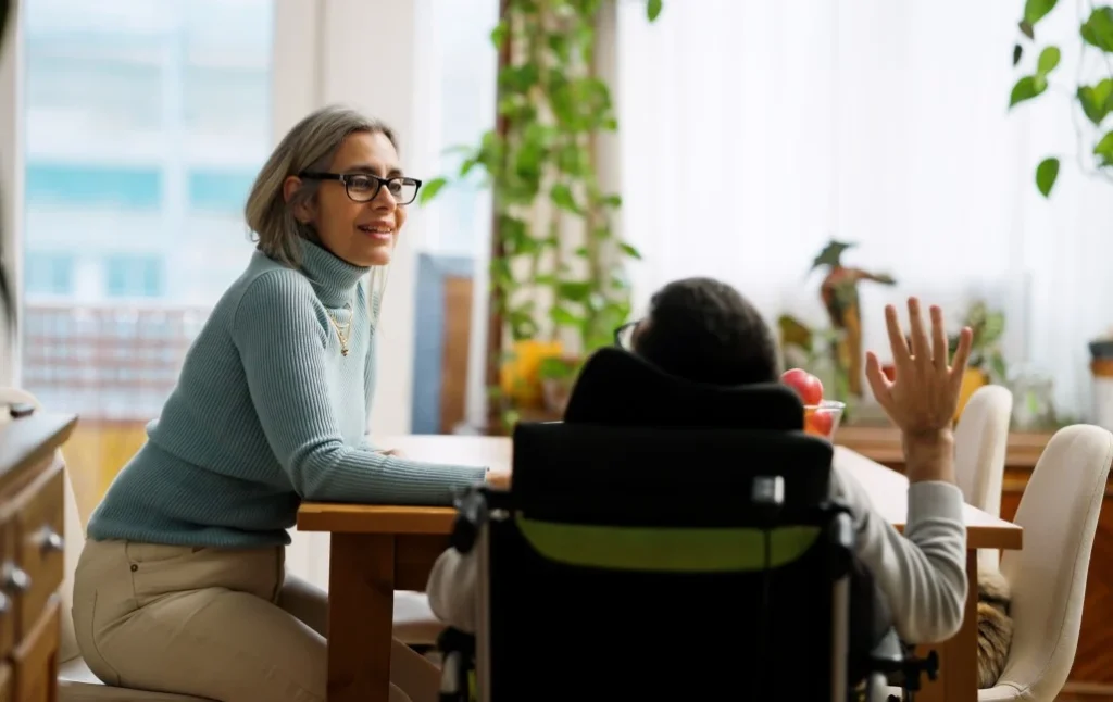 Disabled man in wheelchair talking with support worker at kitchen table